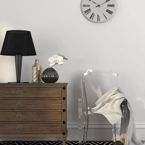 Modern living room with wood dresser, black lamp, decorative vases, transparent chair, and wall clock in simple interior design.