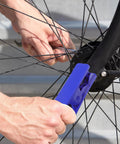 Close-up of a blue bike hydraulic brake hose cutter tool being used on a disc brake near the wheel hub.