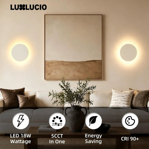 LUXLUCIO Hardwired 9" Round Backlit White Modern Indoor LED Wall Sconce illuminating a cozy living room with artwork.