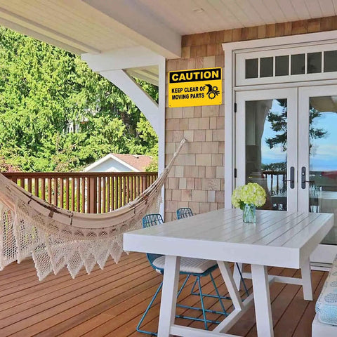 Caution Keep Clear Of Moving Parts 8 By 12 Inch Aluminum Sign for Workshop on porch wall, visible with hammock and table.