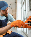 Electrician wearing orange gloves working on a wall socket installation with a screwdriver