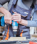 Person using power drill on wood, wearing overalls.