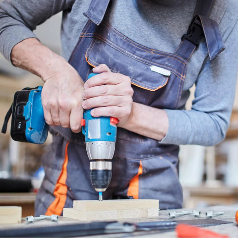 Person using power drill on wood, wearing overalls.