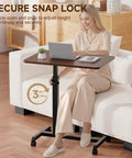 Compact Standing Desk On Wheels With Foldable 24 Inch Desktop Lockable Casters Adjustable Height From 25 To 36.5 Inches Ideal Overbed Or Home Office Laptop Table In Walnut Finish used by woman on sofa