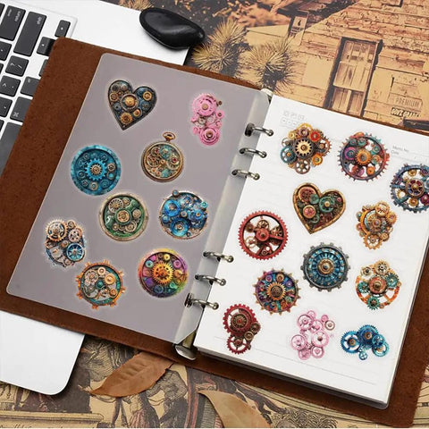 Dope Steampunk Gear Sticker Set 50pc for Journaling with vintage clockwork gears, resin elements, on a notebook next to a laptop.