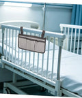 Bed Rail Organizer With Four Pockets And Cup Holder attached to hospital bed rail, grey with dark grey edging, easy strap-on design.