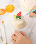 Level Up Your Sweet Baking Game With This Solid Acrylic Cookie Decorating Turntable Kit That Comes Loaded With Scribe Needles Soft Brushes Grip Mats And Rubber Feet For Flawless Icing Every Time. Close-up of hands using scribe needle on a decorated cake.