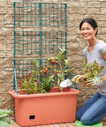Person tending a Movable 58 Inch Self Watering Veggie Planter With Wheels And Trellis For Easy Sun Tracking, outdoor garden