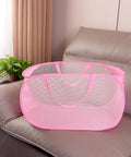 Pink foldable mesh laundry basket pop up hamper with reinforced handles on a sofa, collapsible design for dirty clothes carrier.