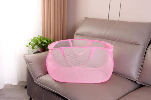 Pink foldable mesh laundry basket pop up hamper with reinforced handles on a sofa, collapsible design for dirty clothes carrier.