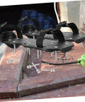 Three pairs of black lawn aerator shoes with metal spikes, surrounded by extra screws, on a workshop table.