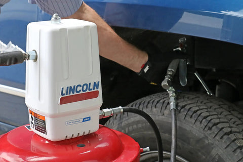 Lincoln 917 Pro Grade 50 To 1 Pneumatic Grease Pump in use, attached to a red base and vehicle tire visible