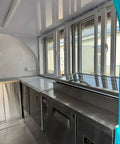 Interior view of Rollout Ready Custom Towable Food Trailer Commercial Mobile Catering Kitchen with stainless steel surfaces and windows.