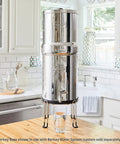 Stainless Steel Stand Lifts Portable Gravity Fed Water Filter Six Inches Above Countertop in kitchen with glass underneath.