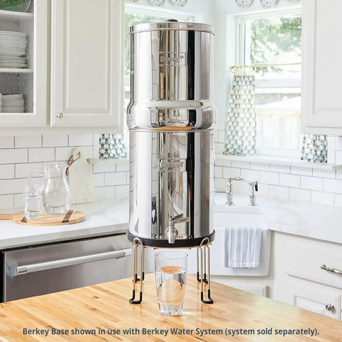 Stainless Steel Stand Lifts Portable Gravity Fed Water Filter Six Inches Above Countertop in kitchen with glass underneath.