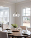 13 Inch Modern Pendant Light With Clear Schoolhouse Glass Shade In Brushed Nickel Finish hanging over dining table with chairs