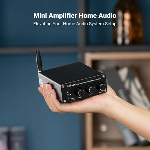 Hand holding Bluetooth Stereo Amplifier 100W Per Channel, 2 Channel Class D Power Amp For Passive Speakers on a bookcase background.