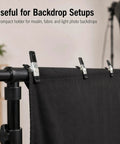 Straight Up Kicking 40 Pack Mini Spring Clamps Heavy Duty Nickel Plated Steel Clips For Quick Crafts Woodworking And Photography Backdrop Holds High Quality Genuine Grip applied to secure black fabric backdrop on a stand.