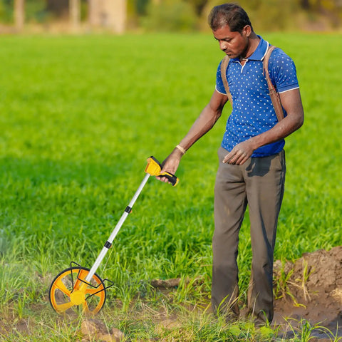 Man using digital measuring wheel with backlit display, pro grade precision to 0.03, in a field, switch between metric and imperial units