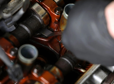Automotive engine valve-train close-up with red cast housing, black hoses, and metal brackets