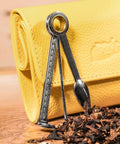 Front view of a stainless steel 3-in-1 pipe cleaning tool (reamer, tamper, poker) with ring handle beside a yellow leather case.
