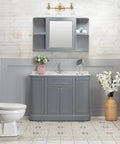 Three Light Vanity Bathroom Light With Clear Glass Shades In Warm Brass Finish above grey vanity in cozy bathroom.