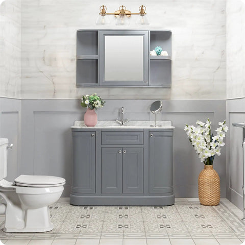 Three Light Vanity Bathroom Light With Clear Glass Shades In Warm Brass Finish above grey vanity in cozy bathroom.