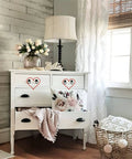 White vintage dresser with tulips, basket, and black knobs, set in cozy living room.