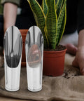 Two Piece Stainless Steel Garden Shovel And Soil Sifter Set next to a potted plant on burlap with blurred background garden scene
