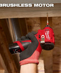Hand holding 12V Subcompact Brushless Impact Driver Bare Tool With Quarter Inch Hex For Tight Spaces under wooden beam.