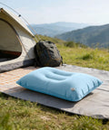 Sky blue inflatable travel pillow with adjustable firmness for custom neck support on a camping mat beside a tent