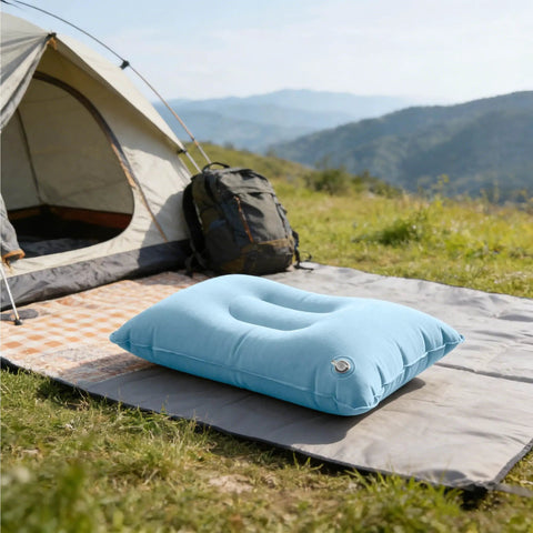 Sky blue inflatable travel pillow with adjustable firmness for custom neck support on a camping mat beside a tent