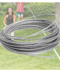 Beefy Five Millimeter Galvanized Zip Line Cable For Backyard Fun Heavy Duty 131 Feet Wire Rope With 1400 Pound Break Strength Flexible 7x19 Steel Cable For Hoist Pulley Wheel And Lifts coiled in front of a blurred backyard scene.