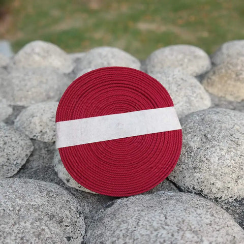 Silk Ito Sageo Wrapping Cord Sixteen Point Four Ft For Katana Wakizashi Samurai Swords on stones, coiled roll of red cord.