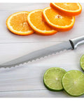 Smooth Serrated Slicer Knife With Knockout Double Sided Teeth That Crush Through Tough Produce Skins Like Hot Knife on countertop next to oranges and limes.