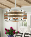5 Light Metal Drum Chandelier With Wood Grain Shade Round Pendant Ceiling Light For Kitchen Island And Dining Room Rustic Farmhouse Style Nickel Finish E26 Base 9 Inch High By 19.7 Inch Wide Includes 47 Inch Chain installed in a bright dining room with flowers and chairs visible underneath.