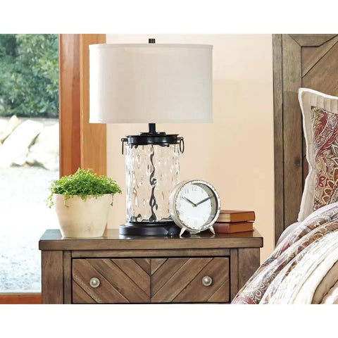Glass Table Lamp With Bronze Finish Base And Fabric Drum Shade on a wooden nightstand in bedroom decor.