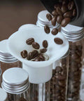 14 Piece Airtight Glass Coffee Bean Storage Tubes With Solid Stand And Hopper Featuring One Way Exhaust Valve Keeps Your Daily Grind Pretty Slick For That Weekend Home Bar Session Countertop Flex with coffee beans being poured