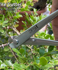 Close-up of a wire cutter from the 6 Piece Bonsai Tool Set Pro Grade With Concave Cutter, 210mm, trimming a plant branch.