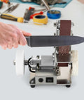 Mini Bench Belt Sander Featuring Slick Adjustable Speed Controls Built Tough As Nails From Stainless Steel Includes Twenty Top Shelf Abrasive Belts To Crush Wood Metal And Knife Polishing Projects Around The Private Garage, with knife being sharpened.