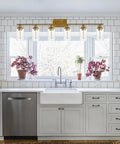 Kitchen view with modern gold vanity light fixture above farmhouse sink, large window, and white cabinetry background