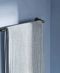 Arris 18 Inch Modern Single Towel Bar Matte Black For Bathroom And Kitchen Use With Easy Install Durable Finish Keeps Towels Handy And Elevates Your Space With Dope Style, holding a striped towel against blue wall.