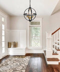 Rustic Farmhouse Chandelier 14-Inch Globe Pendant Light In Vintage Black And Gold hanging in a bright entryway with wooden stairs.