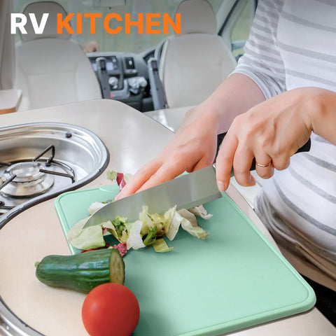 Person chopping vegetables in an RV kitchen using a cutting board and knife, featuring the Camping Cooking Utensils Set 16 Piece Camp Kitchen Kit With Organizer Bag Portable RV Camping Essentials Camper Must Haves For Cookouts And Open Fire Pit.