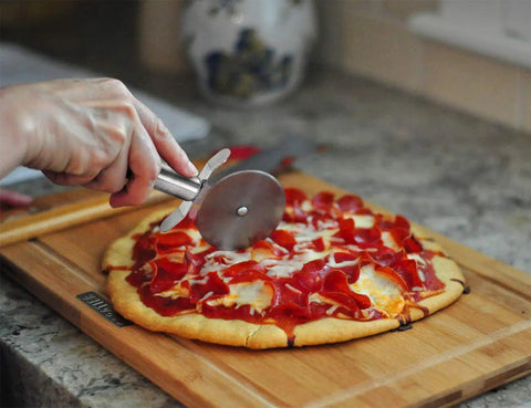 Person using cutter from Pizza Stone Set For Oven And Grill 15 Inch Round Cordierite Stone With 14 By 16 Inch Pizza Peel Stainless Steel Spatula And Cutter Complete 4 Tool Kit For Crispy Crust Bread And BBQ
