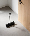 Close-up of a stainless steel hydraulic door closer sitting next to a wooden door, highlighting its no slam quiet soft close feature.