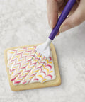 Top Shelf Cookie Decorating Tools Set Featuring Etching Wand Triple Comb And Flexible Silicone Scraper For Bakin Crews crafting royal icing patterns on a cookie.