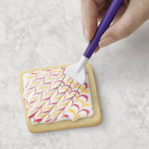 Top Shelf Cookie Decorating Tools Set Featuring Etching Wand Triple Comb And Flexible Silicone Scraper For Bakin Crews crafting royal icing patterns on a cookie.