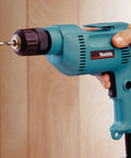 Hand using powerful 4.9 Amp 3/8 Inch Drill with variable speed 0-2500 RPM, keyless chuck, teal finish, drilling wood