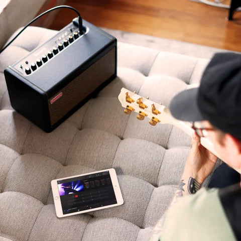 Person using iPad with Spark 40-Watt Combo Practice Amp For Electric Guitar, Bass, And Acoustic With Mobile App on couch
